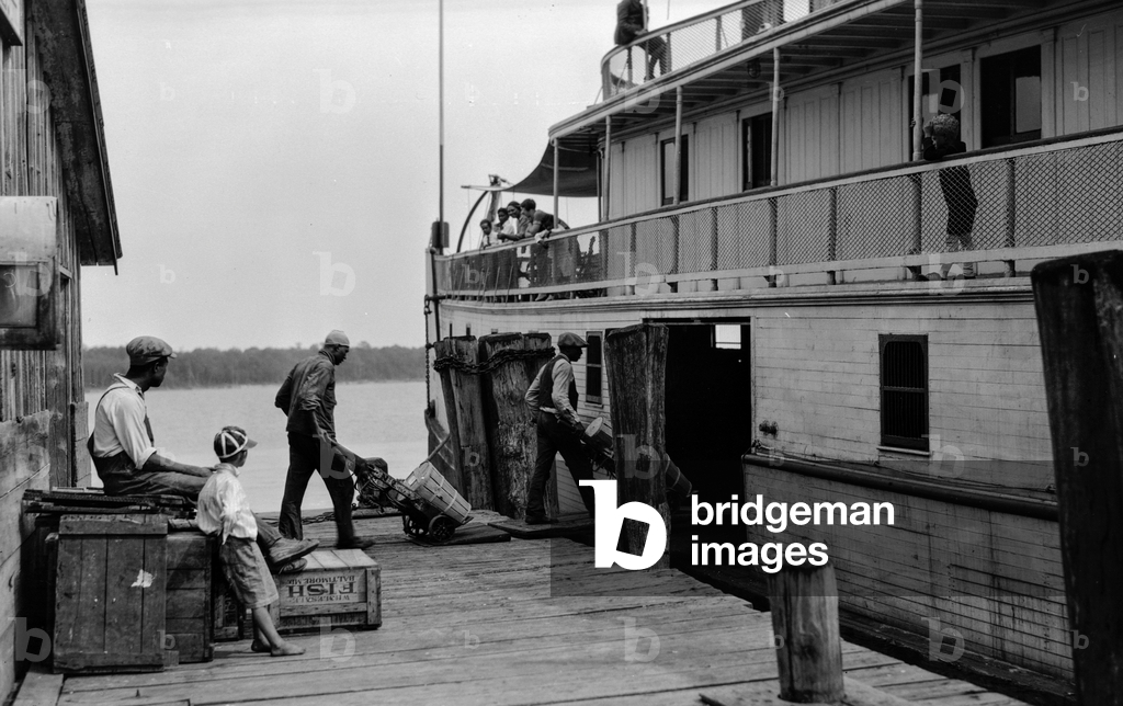 African-American deckhands load barrels and other cargo on a strenwheeler boat on the…, 1929 (photo)