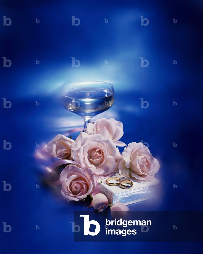 Roses with two wedding rings and the Bible near a wineglass
