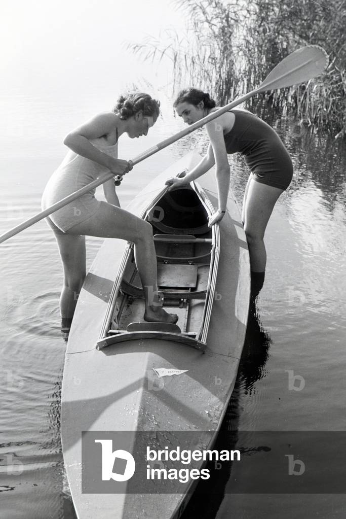 Bild von Fotografie "Zwei junge Frau steigen in ein Boot mit einem Paddel auf einem See"