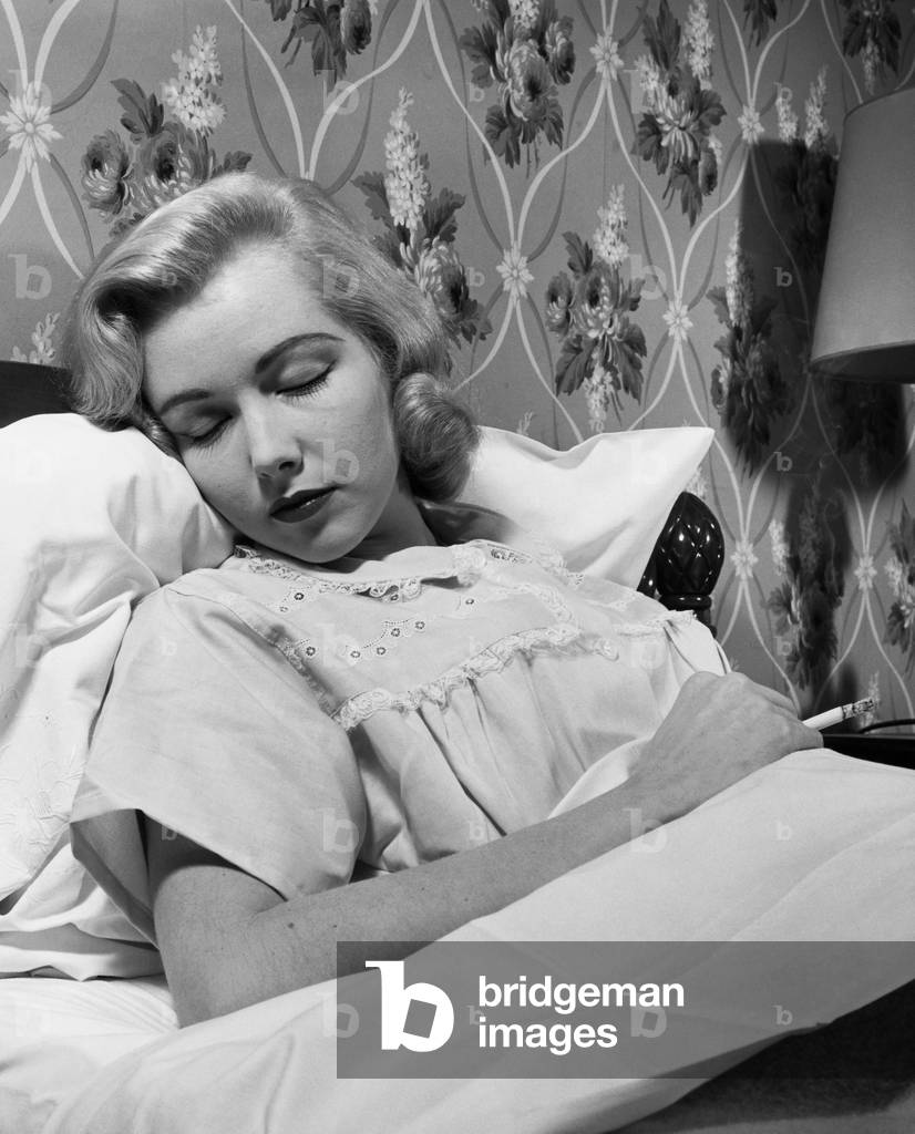 Giovane donna che dorme nel letto e tiene in mano una sigaretta