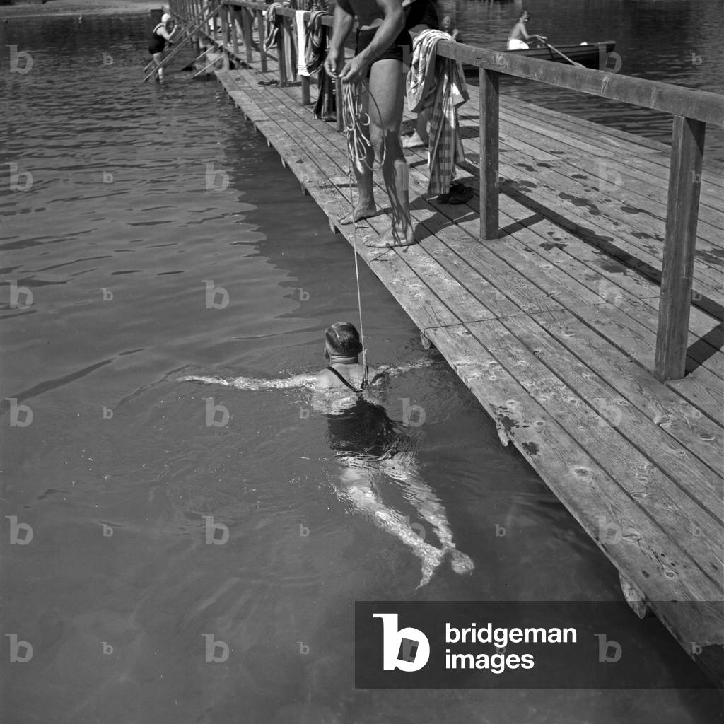 Un addetto alla piscina che aiuta a imparare il nuoto in un lago in Austria, anni 30 (foto in b/n)