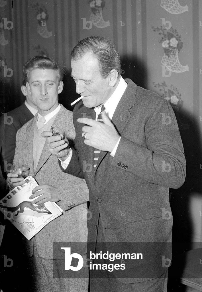 Image of John Wayne in London lighting a cigarette February 1956 (b/w