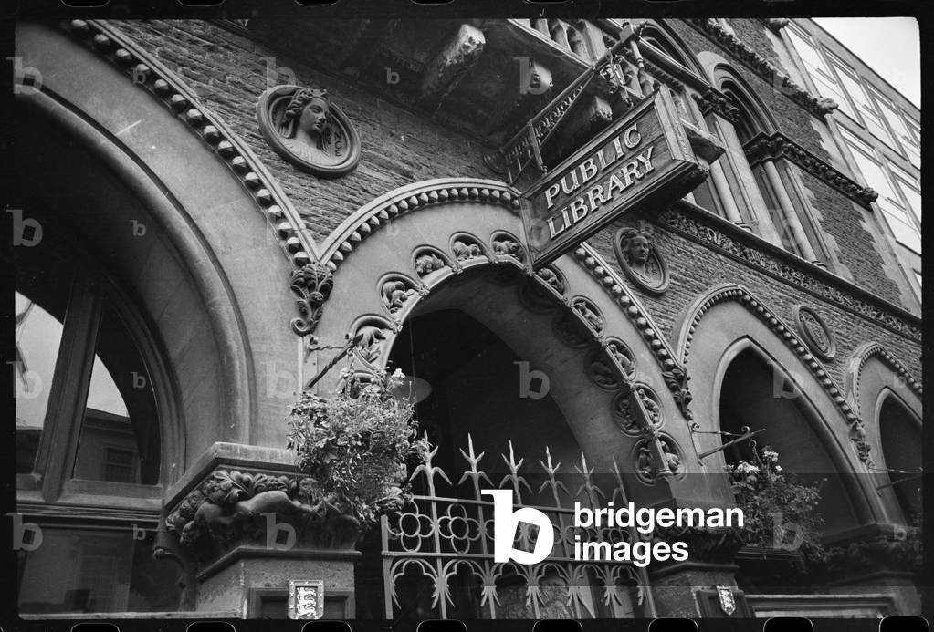 Detailed view of the front facade of the public library, showing the wrought iron gate entrance, round niches 