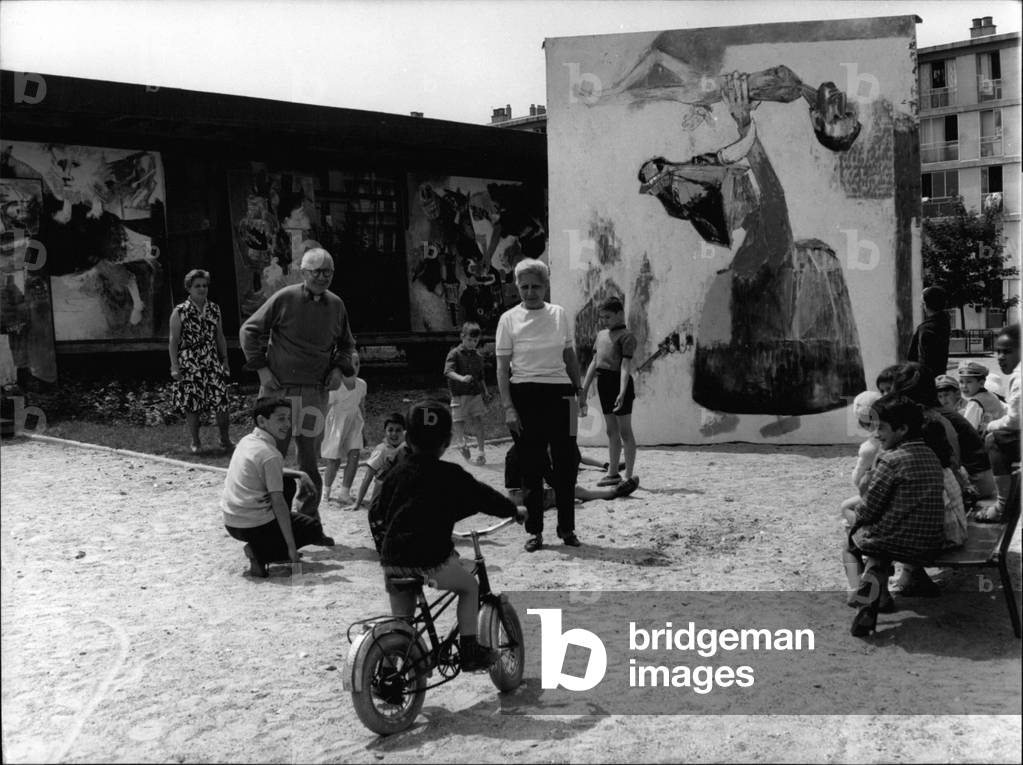 The painter Bernard Lorjou (1908-1986) presents his paintings in the air to the children, with Yvonne Mottet (1906-1968) on June 15, 1965, in Sarcelles, France (b/w photo)