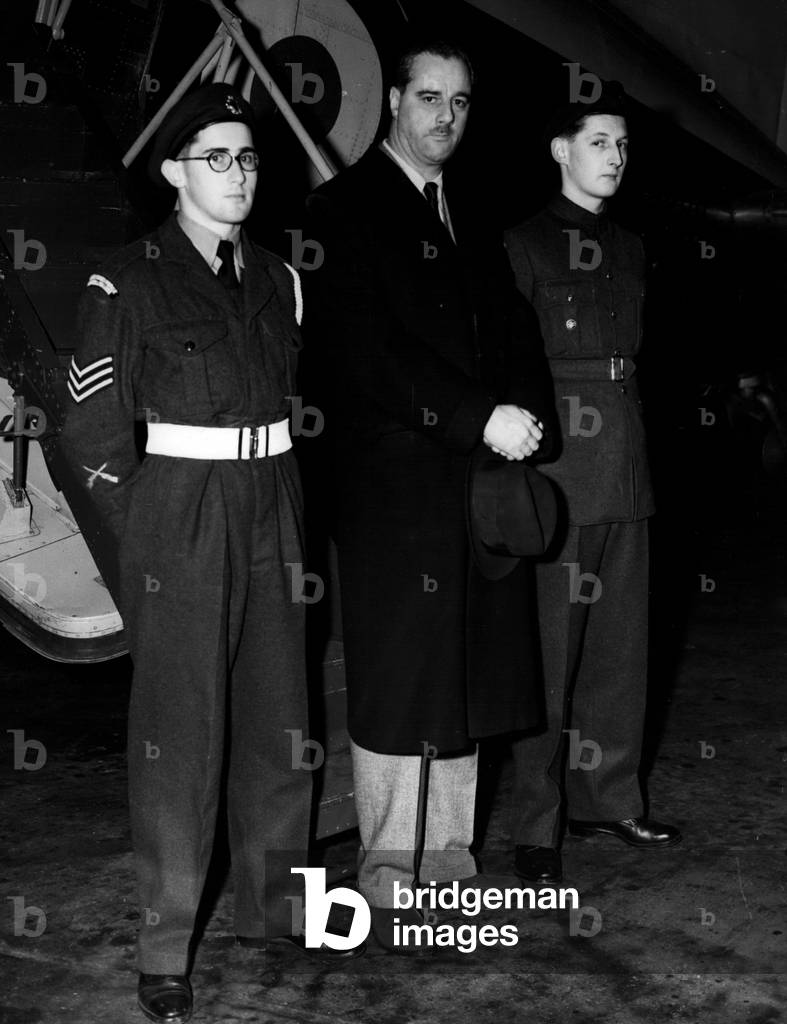 Dec. 12, 1954 - Air Cadets Fly With The Under Secretary Of State For Air: When Mr. George Ward, M.P. Under secretary of State for Air left London Airport this morning for a tour of Royal Air Force unites in the Middle East, m two young cadets flew with him. Chosen From more than 40,000 Air Cadets in the United Kingdom, they will act as assistant air quartermasters in the Heating aircraft. They are, Cadet Harley Brian Hall, 17, of Bexley, Kent, and member of No. 1227 A.T.C. Squadron at Christchurch and Sidcup County Grammer School, who is hoping go tothe R.A.F. College at Cranwell, abnd Cadet Dan Villiers Dalap, 17, of “Clan Connal”. Manorway., Lee-on-Solent, Hants - a member of the Campbell College Combined Cadet Force, Norway Ireland, whose father is a former wing commander in the R.A.F. The 11,000 flight will take the boys over the Mediterranean to Cyprus and then on to Jordan Iraq, Bahrain and Trucial Okman state (Persian Gulf), Aden, Nairobi, Khartoum and the Canal Zone before retuning via Cyprus and Idris (Libya). It will last three week and is regarded as a special regard to the cadets for proficiency,;. Phot Shows Mr. George Ward, with the two Cadets, Cadet Dan Villiers Delap (left), and Cadet Harley Brian Hall (right), prior to departure