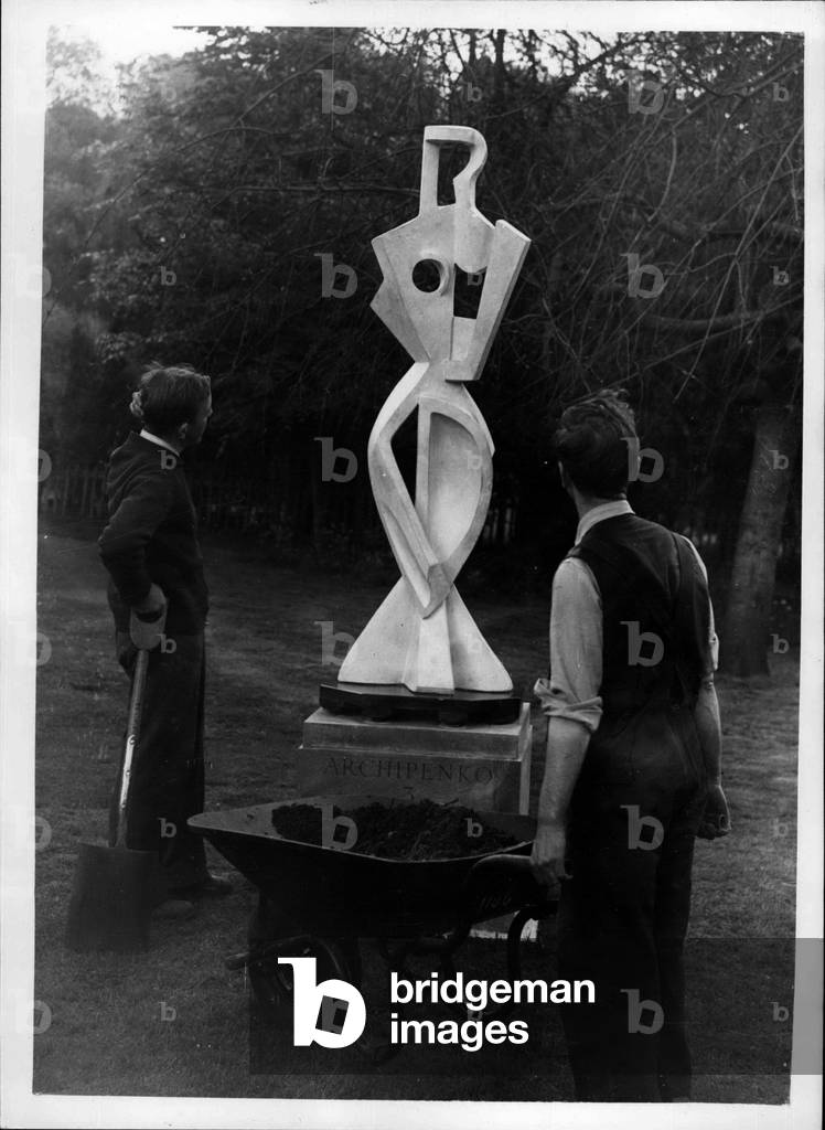 May 25, 1954 - A Puzzle - In The Park Open Air Sculpture Exhibition: Photo show Two gardeners are very puzzled over this creation - whch has bnee named” The standing woman”. It is one od the exhibits bu Alex Archipenko at the exhibition of sculptutre in Holland Park, London, organiased buy the London Country Council