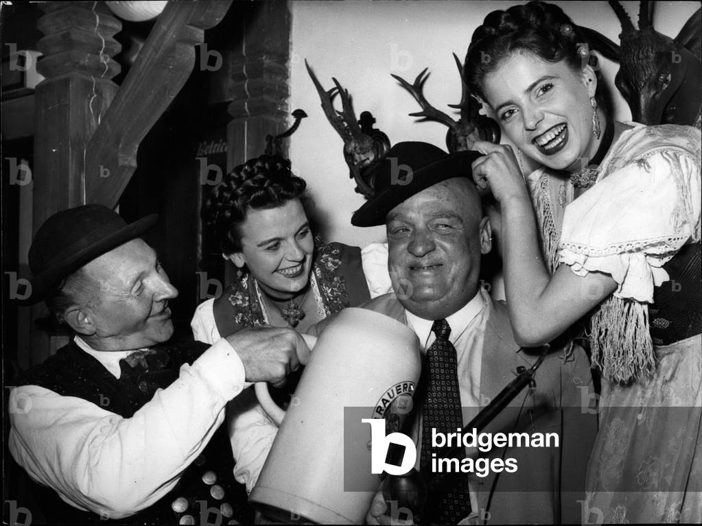 Sep. 09, 1953 - Dr. John Billweiler from Basle will be able to visit the Munich:” Platxzl” (an original Bavarian amusement place) for life without having to pay an entrance fee. Dr. Billweiler, the inventor of the liquid coal and also founder of the famous Leuna-works, was the 100,000 visitor of this world-known Munich amusement place after its re-opening on March 25th, 1953. The Platzl-actors Karl Baierl, Christl Hoeck and Gerda Staiener handed over to Dr. Billweiler an oversized beer-jug, and entry-ticket for life and topped him up with an original Dachau costume hat.